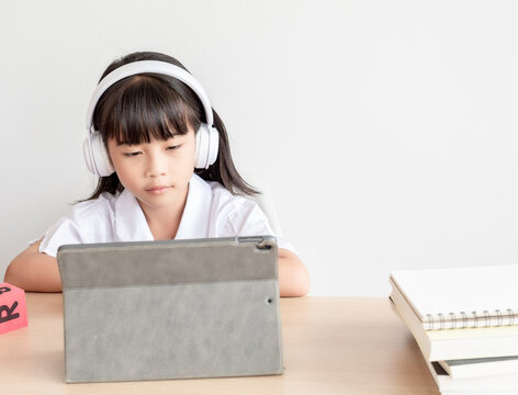 A Chinese elementary school girl is taking online classes at her desk. 