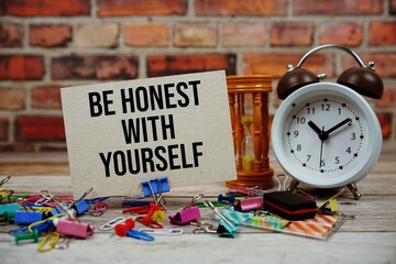 Be honest with Yourself text on paper card with alarm clock and stationary on wooden background