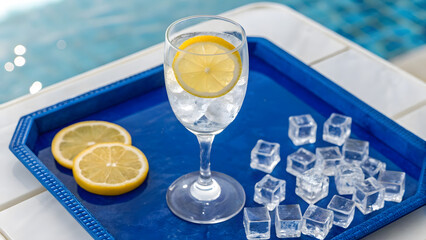 Refreshing drink with lemon slices on a blue tray by the pool on a sunny day