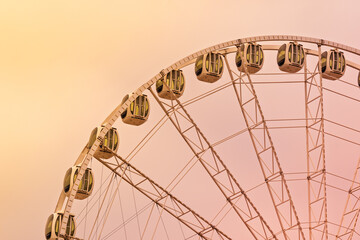 Modern ferris wheel with glass cabins at sunset, illuminated by warm light and pastel sky.