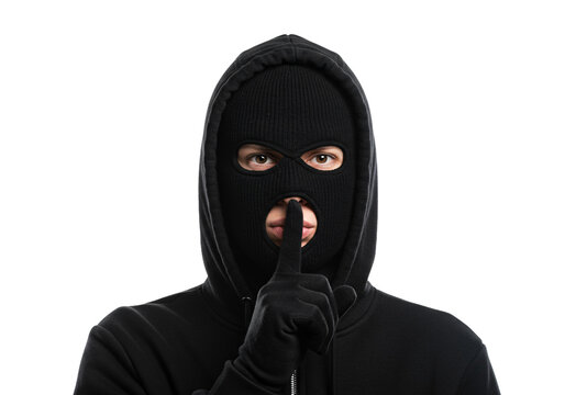 A person wearing a black balaclava and hoodie holding a finger to their lips in a shushing gesture isolated on transparent background - Powered by Adobe