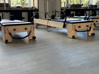 Side angle of Pilates reformers positioned near windows in a naturally lit studio. The image highlights structure, light wood materials, and strong afternoon shadows.
