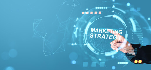 Businessman hand pointing at digital interface with text "Marketing Strategy" on futuristic blue background, representing modern business concept.