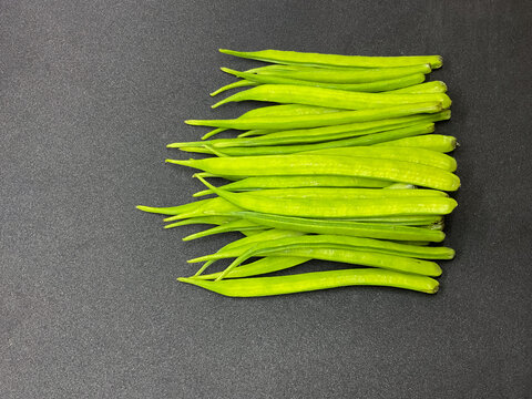 A pile of legumes, cluster beans also known as guar beans or guar pods on dark gray background 