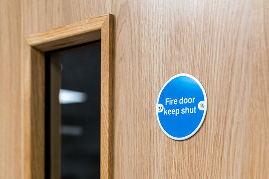 Close-up of a typical Fire Door Keep Shut sign seen on an interior door within a British hospital. The firedog prevents any fire or smoke spreading in the building.
