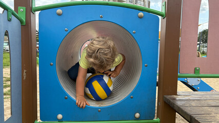 Child exploring playground tunnel with a volleyball. Active outdoor play, focus and motor...