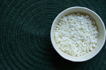 A white cup with cottage cheese stands on the right on a green background