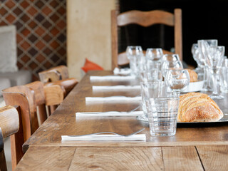Grande table en bois dressée pour un repas de fête, avec verres, couverts et pain artisanal