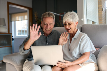 Happy senior couple video calling family with laptop at home