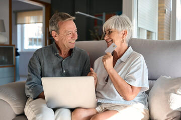 Happy senior couple shopping online using laptop and credit card at home
