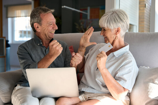 Happy senior couple shopping online using laptop and credit card at home