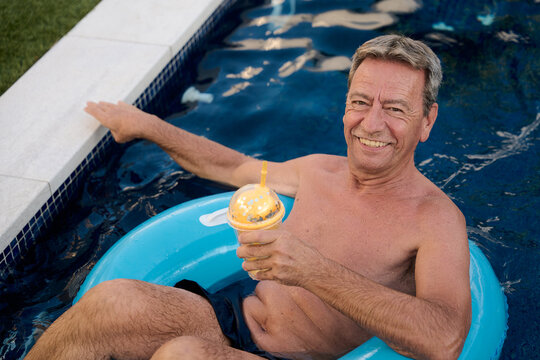 Senior man relaxing in pool with inflatable ring and tropical drink