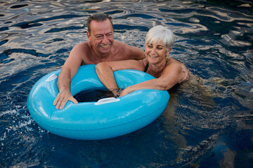 Happy senior couple having fun with inflatable ring in swimming pool