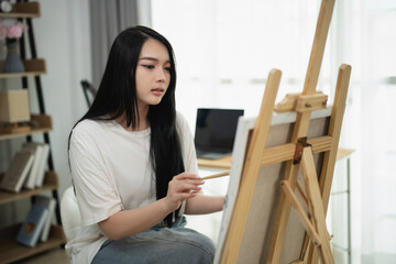 Young woman artist concentrating on creating a painting in a bright indoor space with natural light and modern decor style