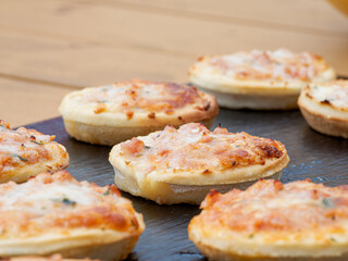 Mini pizzas apéritives disposées en rang sur une ardoise noire lors d’un buffet d’extérieur, ambiance conviviale