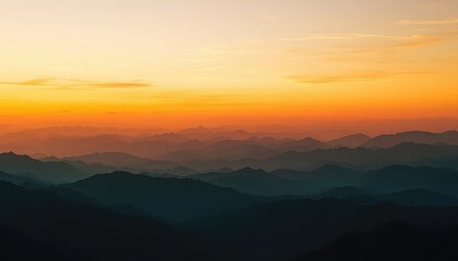 Fototapeta premium Dramatic layers of shadowy mountains recede into the distance beneath a bright orange and yellow sky at sunset