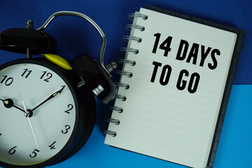 14 Days To Go text written on notebook paper with alarm clock