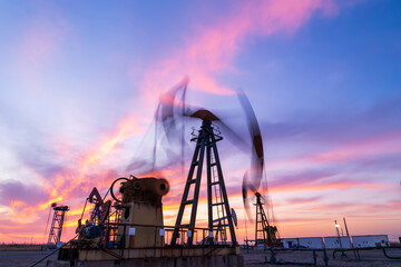 in the evening, oil pumps are running, The oil pump and the beautiful sunset reflected in the water, the silhouette of the beam pumping unit in the evening.