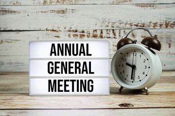 Annual General Meeting text on light box with alarm clock on wooden background