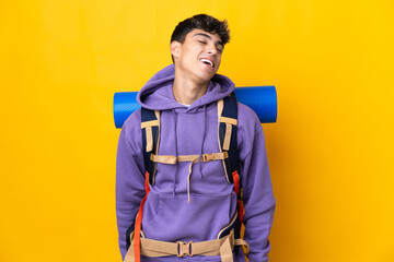 Young mountaineer man with a big backpack over isolated yellow background laughing