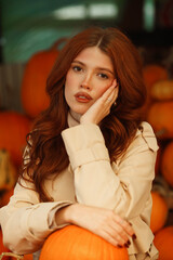 Portrait Beautiful red-haired young woman sits at the counters with oranges at the city vegetable market. Autumn and Halloween season.