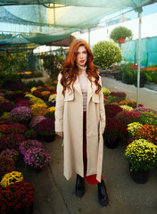 Portrait Beautiful red-haired young woman in beige trench coat at city flower Autumn market.