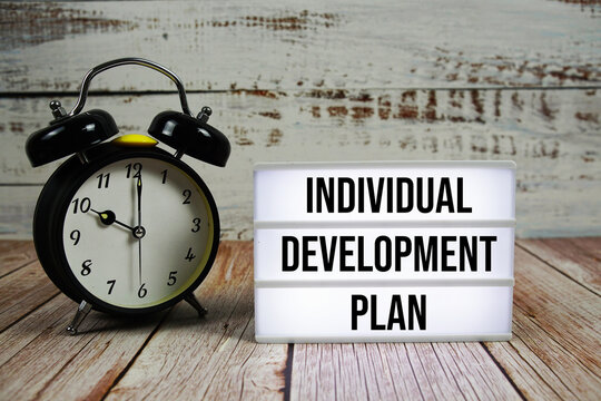Individual Development Plan text on light box with alarm clock on wooden background - Powered by Adobe