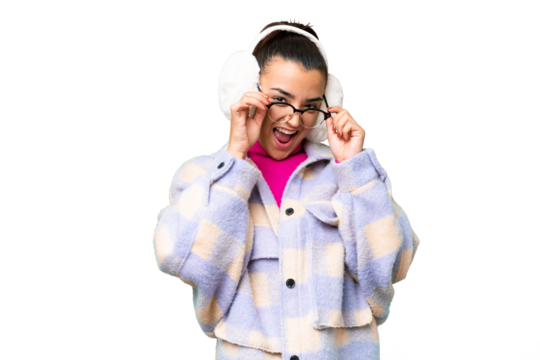 Young woman wearing winter muffs over isolated chroma key background with glasses and surprised