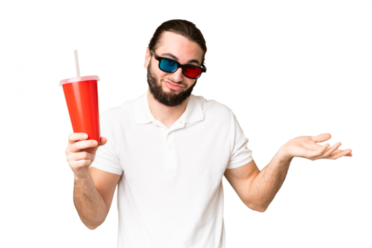 Young handsome man holding soda while watching a 3D movie over isolated chroma key background making doubts gesture while lifting the shoulders