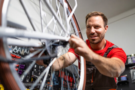 Caucasian serviceman repairing bicycle wheel in workshop. - Powered by Adobe