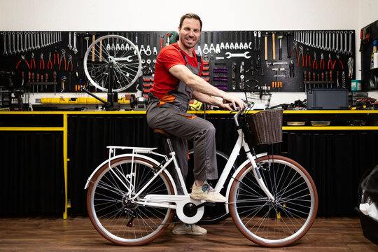 Professional bicycle service and repair shop. Experienced mechanic sitting on bicycle inside repair shop.