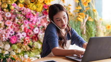Asian adult woman managing artificial flower shop customer orders using laptop and phone call for digital sales