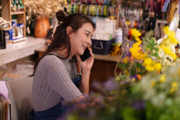 Asian woman business owner engages customers through phone calls managing her artificial flower shop daily operations and sales