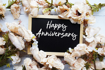 Happy Anniversary text with flower decoration on wooden background