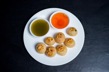 Delicious north and south indian street food pani puri gol gappa with tamarind water served in white plate and potato and chickpeas
