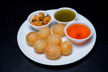 Delicious north and south indian street food pani puri gol gappa with tamarind water served in white plate and potato and chickpeas