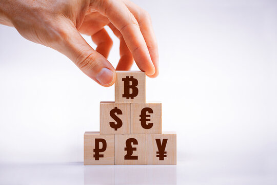 A hand places a Bitcoin cube on top of a pyramid of world currencies, symbolizing the dominance of cryptocurrency, financial innovation, and the future of digital money
