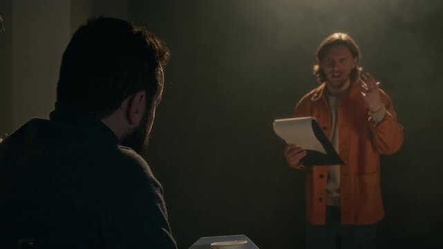 Actor reading script and performing scene for unrecognizable filming director during acting audition in dimly lit studio