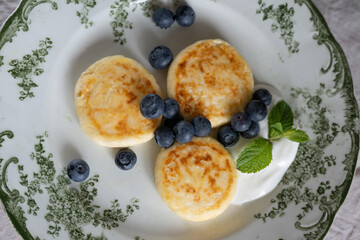 Three golden cheesecakes are served on beautiful vintage plate with fresh blueberries, sour cream and mint leaf
