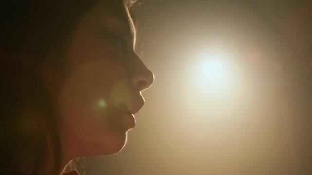 Close-up shot of young actress saying her lines while performing scene on dimly lit set with dramatic lighting