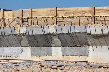 A detailed view of a bridge shows concrete forms, exposed steel reinforcement bars, and wooden formwork under bright sunlight, highlighting early construction and civil engineering processes