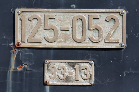 Two metallic identification plates, marked "125-052" and "33-13", are mounted on a worn and rusted train surface, indicating locomotive and component identification codes