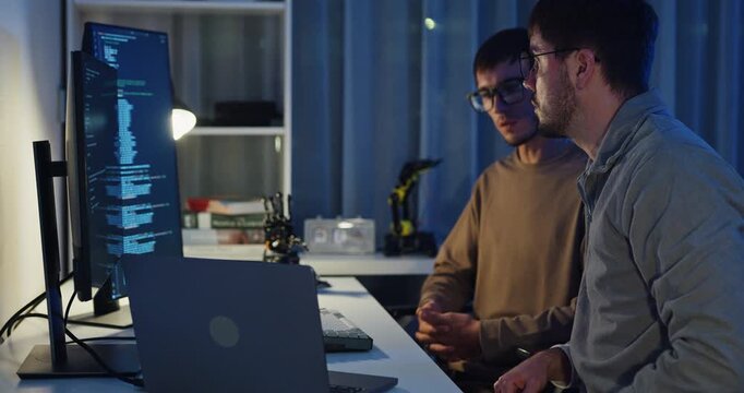 Team adult male engineer collaborate on robotic hand project using AI code solutions machine learning at tech workspace night. Artificial intelligence interface, collaboration prototype development.