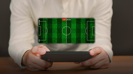 Football fans watch a live football match on a smartphone screen with a green football field background. Concept of online sports streaming, digital entertainment, or live sports broadcast at home.