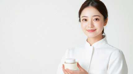 Woman white uniform holding skincare product jar, smiling warmly against plain white background. image conveys sense of professionalism, green marketing, and environmental awareness, promoting eco