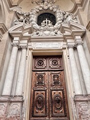 Elegant Baroque Church Portal with Sculpted Angels and Wooden Doors in Parma, Italy.The architectural detail includes angels, cherubs, and classical columns, representing a fine example of Italian Bar