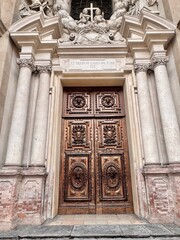 Obraz premium A beautifully detailed Baroque church entrance in Parma, Emilia-Romagna, Italy. The scene features finely carved wooden doors, classic stucco columns, and expressive angelic sculptures above, crowned.