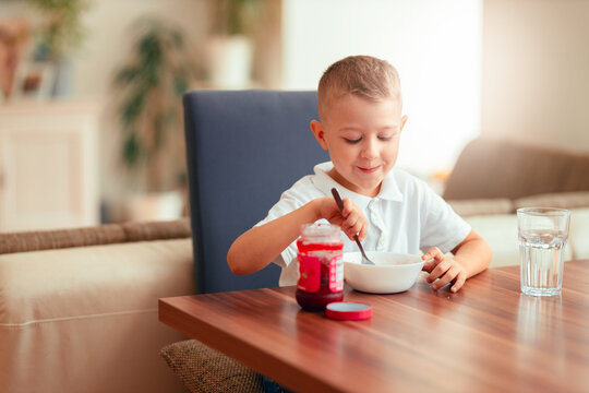 Cute 5-year-old boy having breakfast at home, eating porridge with jam.