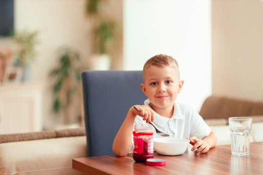 Cute 5-year-old boy having breakfast at home, eating porridge with jam.