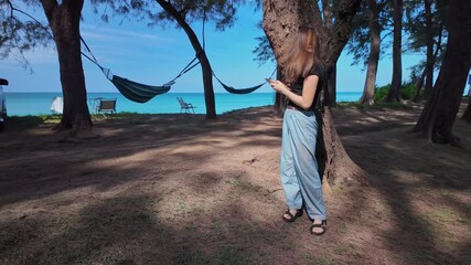 Slow motion video of young woman walking along the beach holding a phone under the shade of a pine tree by the sea.A large tunnel of pine trees along the beach catches the eye
beautiful natural place - Powered by Adobe